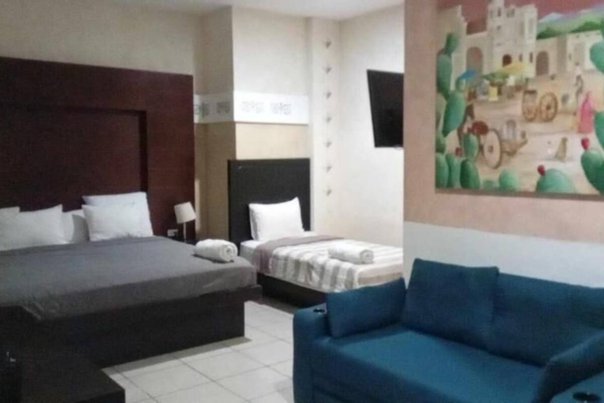 A hotel room with a large bed, a smaller bed, a blue sofa, and a wall painting.