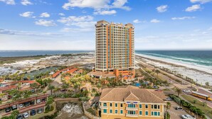 A high-rise hotel with multiple balconies, a beach view, and a parking area with a bus.