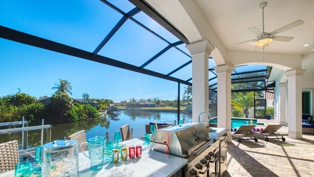 An outdoor bar with a grill, lounge chairs, and a view of a lake.
