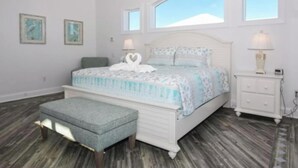A bedroom with a bed, a nightstand, a bench, and two windows. - "Seas the Day" (Week or Month) on Ormond Beach with  Pool and Ocean Views (Ormond Beach)