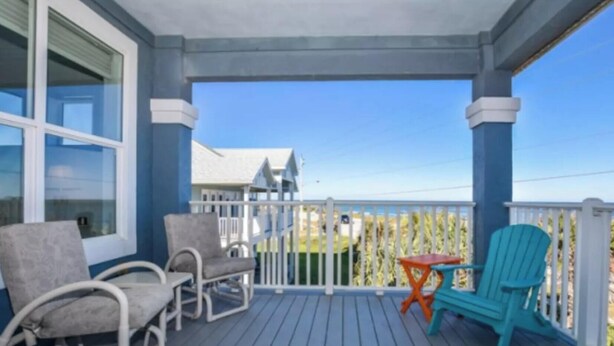 A covered porch with two chairs and a small table, overlooking a residential area. - "Seas the Day" (Week or Month) on Ormond Beach with  Pool and Ocean Views (Ormond Beach)
