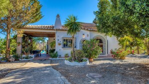 A house with a tiled roof, a covered patio, and a garden with various plants and a palm tree.