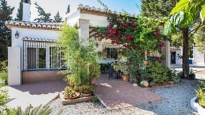 A house with a patio, surrounded by various potted plants and a small garden area.