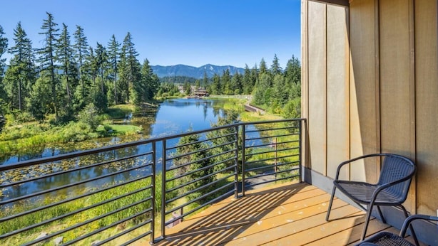 Un balcon donnant sur une rivière, entouré d’arbres et de montagnes.