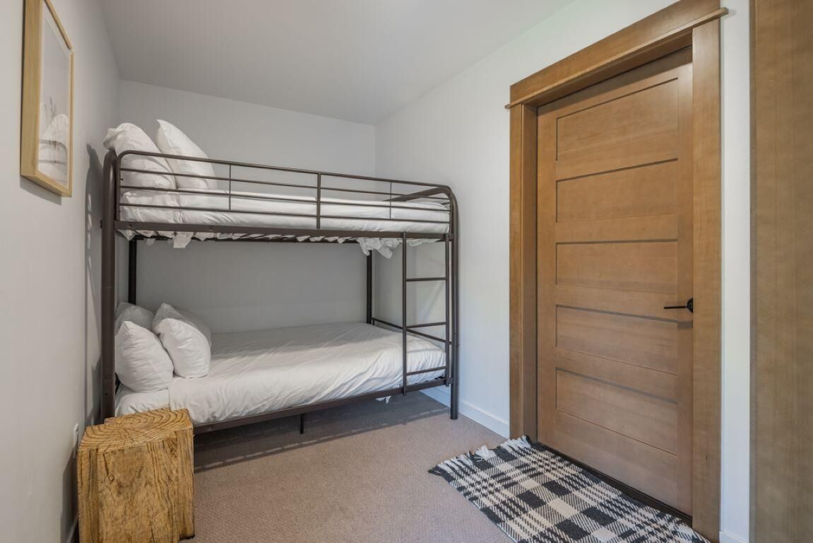 Une chambre avec un lit superposé, une porte en bois et un petit tabouret en bois.
