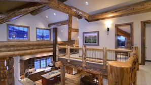 A rustic interior with exposed wooden beams, a dining area, and a view of a snowy landscape through large windows. - Red Feather Ranch (Crested Butte)
