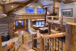 A spacious log cabin interior with a central island, wooden railings, and large windows.