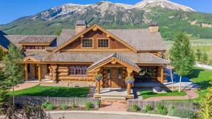 A log cabin with a stone foundation, a covered front porch, and a mountain backdrop. - Red Feather Ranch (Crested Butte)