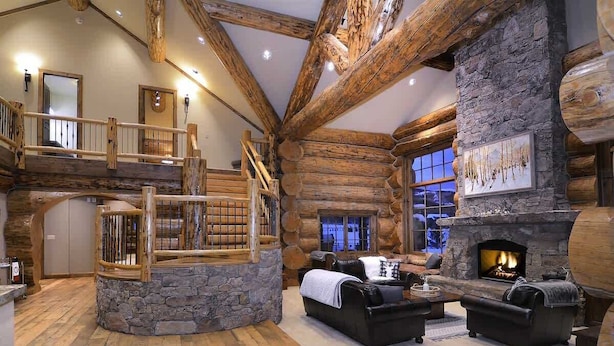 A log cabin interior with a stone fireplace, a wooden staircase, and a cozy seating area. - Red Feather Ranch (Crested Butte)