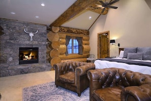 A log cabin bedroom with a stone fireplace, leather furniture, and a large bed.