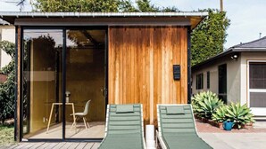 Ein moderner Außenbereich mit einer Lounge-Ecke, zwei grünen Sitzmöglichkeiten und einem kleinen Tisch, einer Holzwand und einer Glastür, die zum Innenbereich führt.