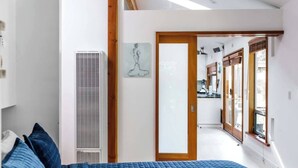 Ein Schlafzimmer mit einem Bett, einem Lüftungsgitter, einer Tür zu einem Badezimmer und einem Fenster.