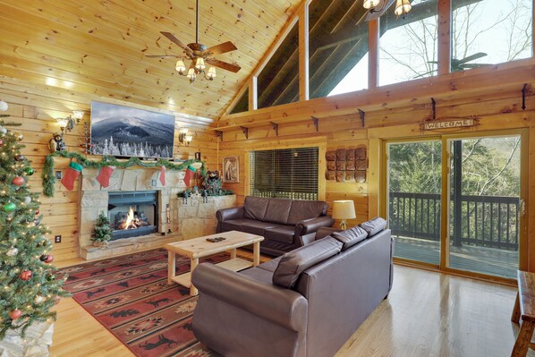 A cozy cabin interior with a fireplace, leather sofa, and a Christmas tree.