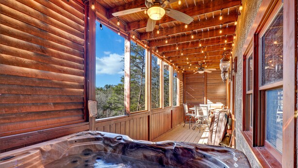 A wooden cabin with a hot tub and a deck with outdoor furniture.