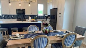 A modern kitchen with white cabinets, a central island, and a dining area with striped chairs and a wooden table.