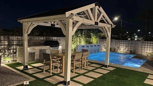 A covered outdoor kitchen with a grill, dining area, and a hot tub.