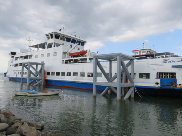 Un ferry grande atracado en un muelle, con una embarcación más pequeña al frente.
