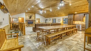 Ein geräumiger Essbereich mit einem großen Holztisch und Bänken, eine gemütliche Sitzecke mit einem braunen Sofa sowie eine Küche mit Holzschränken und einem Geschirrspüler.