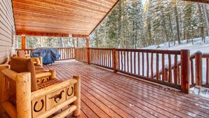 Eine Holzterrasse mit überdachter Sitzgelegenheit und Blick auf einen verschneiten Wald.