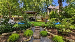 A garden with a gazebo, seating area, and a stone pathway leading to a pool.