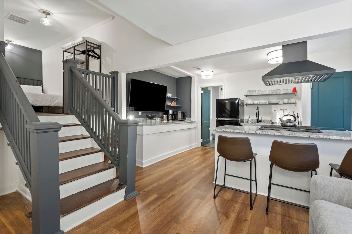 A modern kitchen with a central island, bar stools, and a staircase leading to a bedroom.
