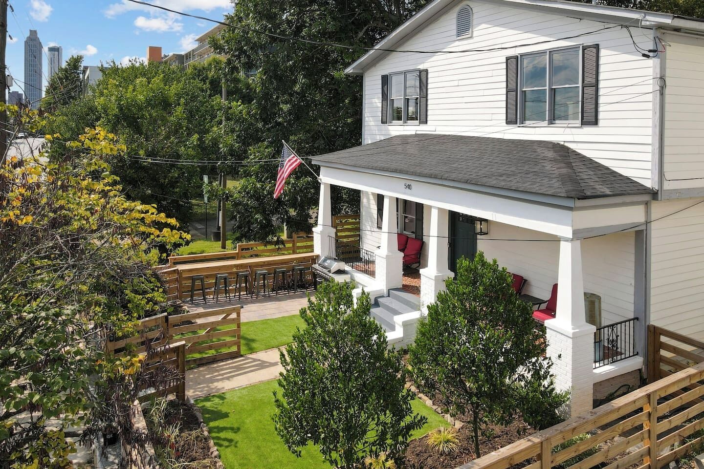 A two-story house with a covered porch, a flag, and a view of a city skyline.