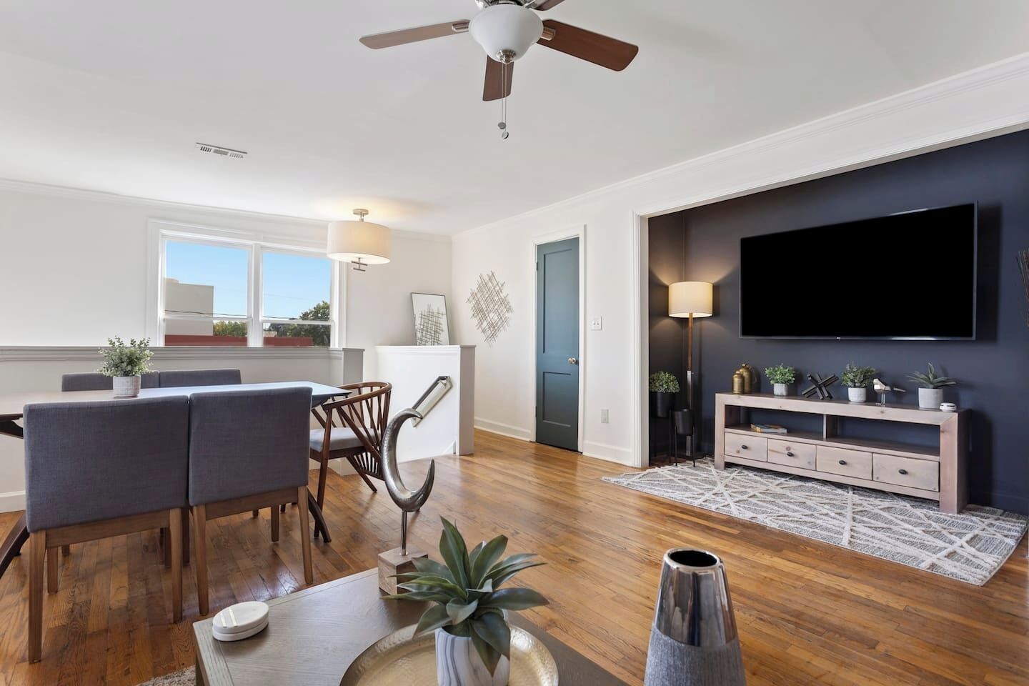 Un salon moderne comprenant un coin repas, un téléviseur fixé au mur et un ventilateur de plafond.
