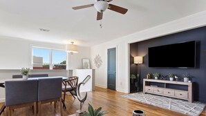 Ein modernes Wohnzimmer mit Essbereich, einem an der Wand befestigten Fernseher und einem Deckenventilator.