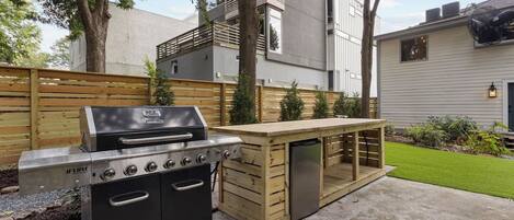 Un espace cuisine extérieur doté d’un barbecue intégré et d’une table en bois.