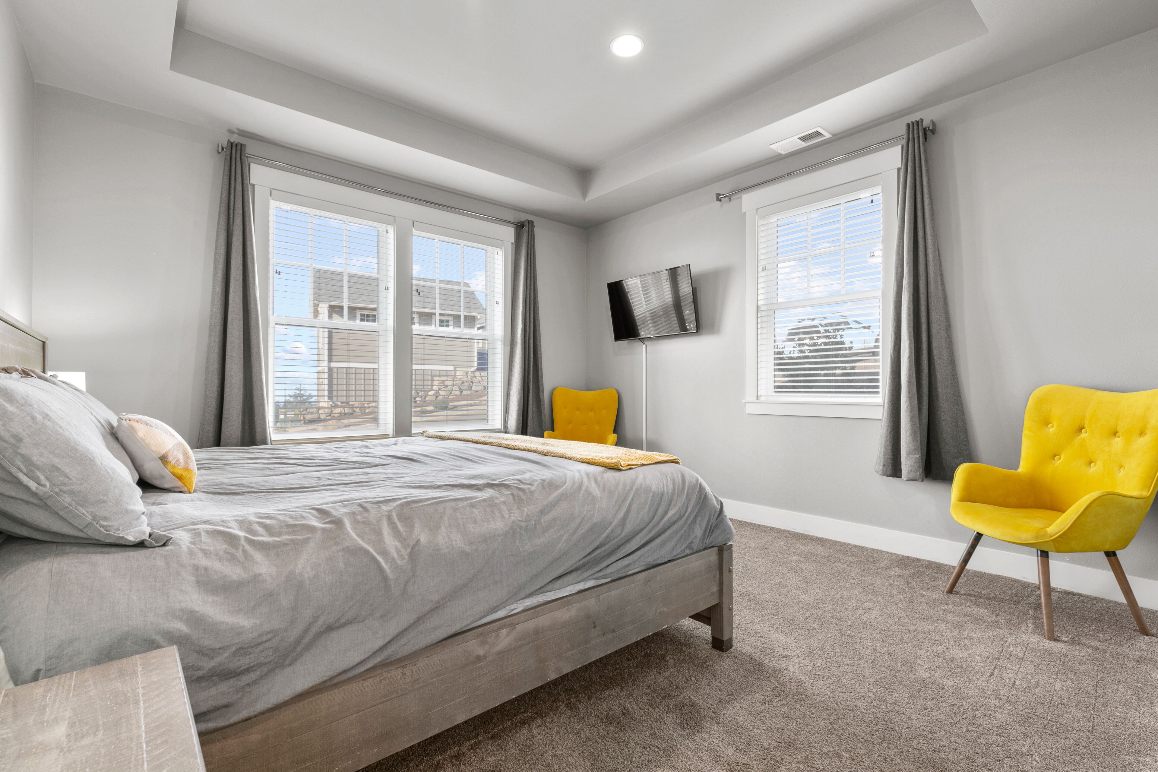 A modern bedroom with a bed, a TV mounted on the wall, and a window with curtains.