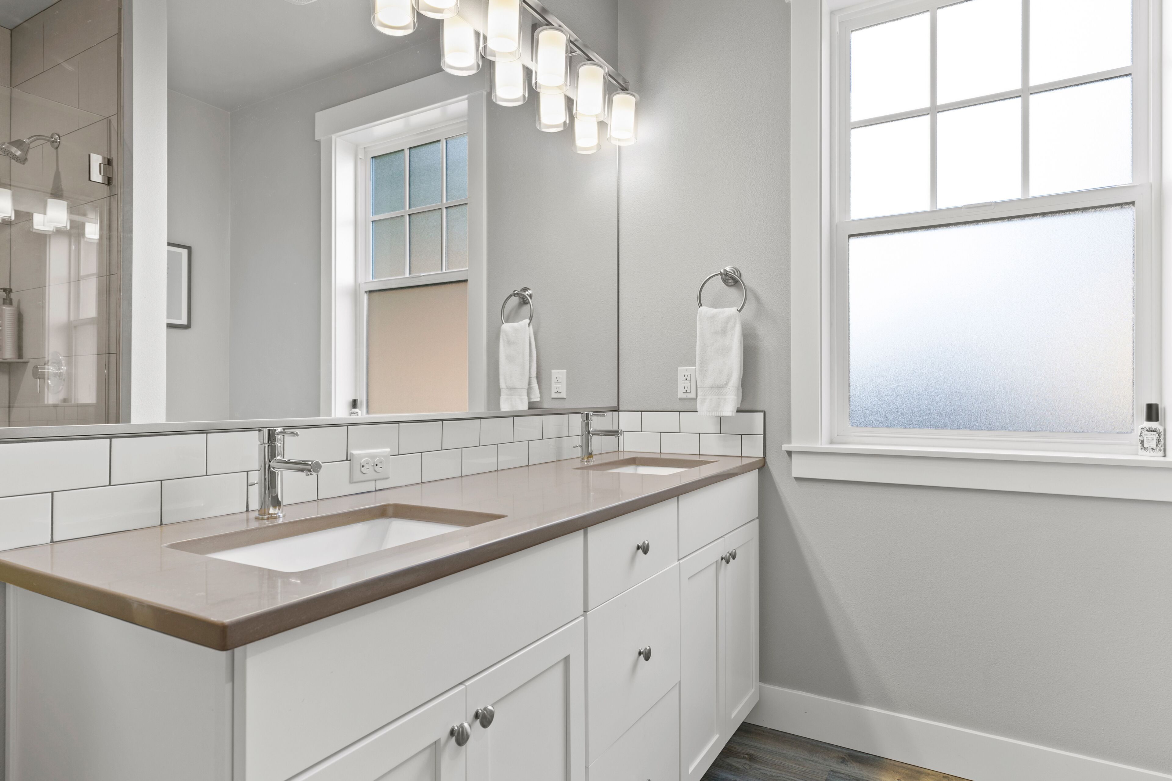 A modern bathroom with two sinks, a large mirror, and a window with frosted glass.