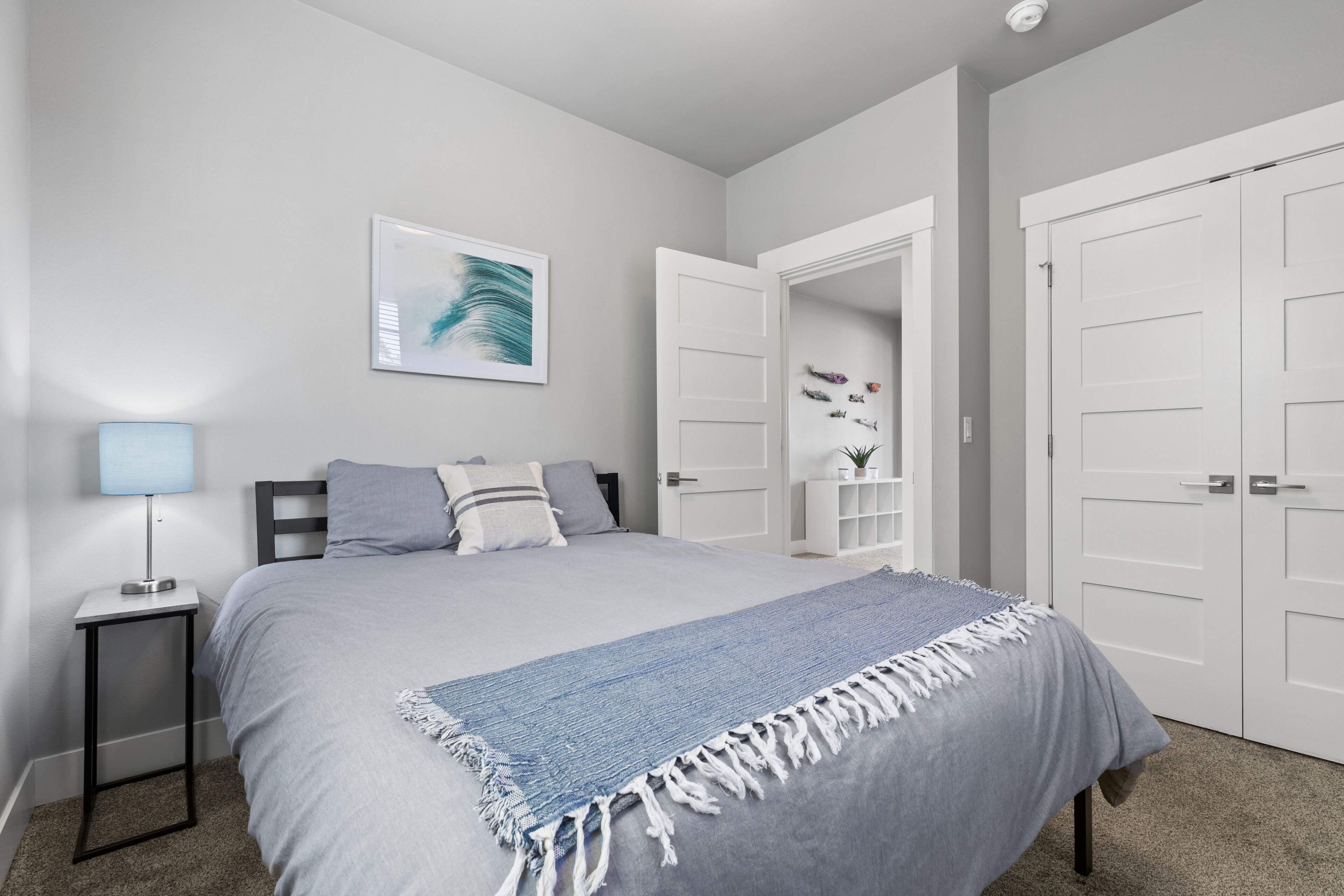 A bedroom with a bed, a nightstand, a lamp, a wall art piece, and a closet.