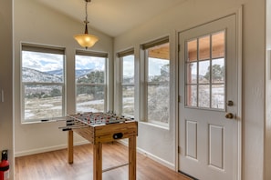 Enjoy a scenic view from the large windows in this inviting space, featuring a foosball table and a ceiling light fixture.