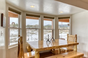 Enjoy meals in this dining area with a large table and benches, adjacent to windows offering a view of the surrounding landscape.