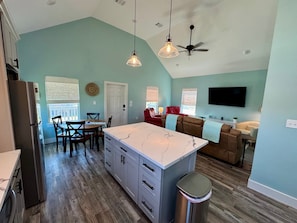 A spacious kitchen with a marble island, a dining area with wooden chairs, a ceiling fan, and a TV mounted on the wall.