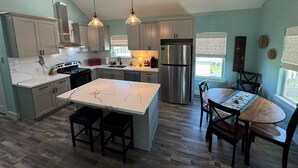 A modern kitchen with marble countertops, stainless steel appliances, and pendant lighting. - The Sea Glass Retreat - Surfside Beach Texas (Freeport)