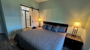 A bedroom with a bed, two bedside lamps, a nightstand, a sliding door, and a wooden floor. - The Sea Glass Retreat - Surfside Beach Texas (Freeport)
