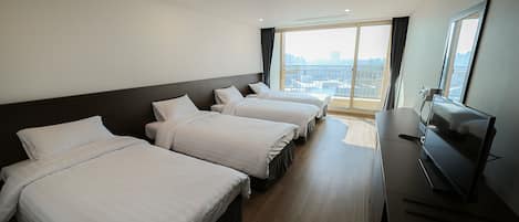 A hotel room with three beds, a TV, and a large window offering a city view.