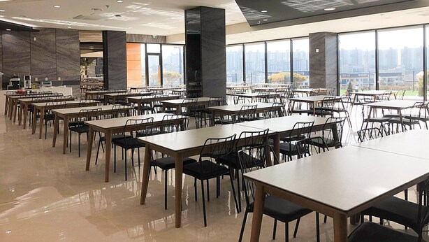 Een ruime eethoek met meerdere tafels en stoelen, grote ramen met uitzicht op de stad en een modern plafondontwerp.