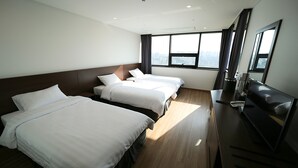 Een hotelkamer met drie bedden, een bureau met een computer en een groot raam met uitzicht op de stad.