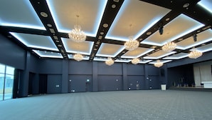Een ruime vergaderzaal met een hoge plafond, meerdere kroonluchters en een vloerbedekking.