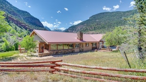 Ein Chalet mit Steinverkleidung, großen Fenstern und einem roten Dach, umgeben von Bergen und einem Holzzaun.