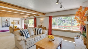 Ein Wohnzimmer mit einem beigefarbenen Sofa, einem Holztisch und einem großen Fenster mit roten Vorhängen.