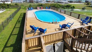 Een houten terras met een zwembad, omringd door blauwe stoelen, en huizen op de achtergrond.