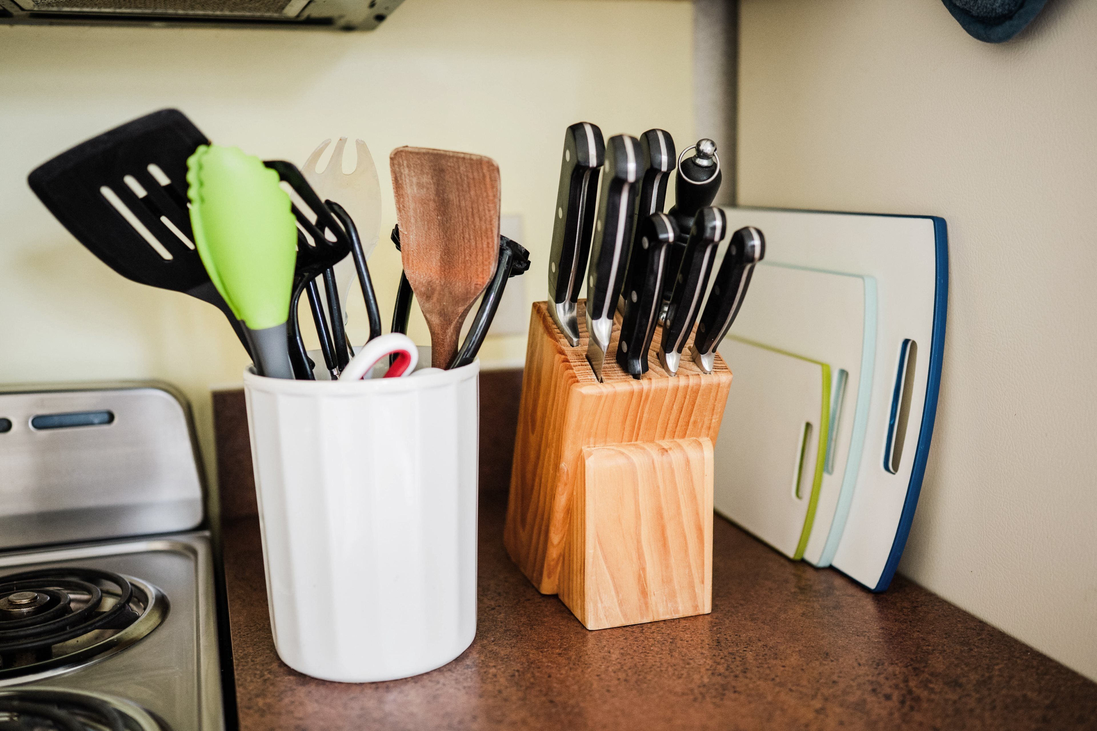 A kitchen counter with a white utensil holder and a wooden knife block.