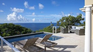 Área de piscina con sillas de descanso y vista al océano.