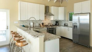 Una cocina moderna con armarios blancos, encimera de granito, electrodomésticos de acero inoxidable y una zona con taburetes de bar.