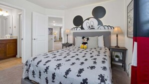 A bedroom with a Mickey Mouse themed bedspread, a nightstand with a lamp, and a Mickey Mouse plush toy on the bed. - Windsor Island Pool Home | Rare Backyard Privacy | 3 Master Suites | Game Room (Davenport)