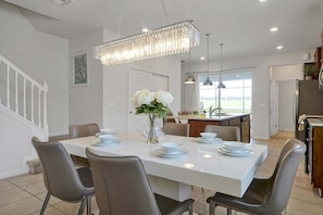 A modern kitchen with a dining area, featuring a large island, pendant lighting, and a view to the outdoors. - Windsor Island Pool Home | Rare Backyard Privacy | 3 Master Suites | Game Room (Davenport)