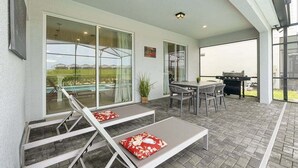 A covered patio area with a pool, lounge chairs, a table, and a grill. - Windsor Island Pool Home | Rare Backyard Privacy | 3 Master Suites | Game Room (Davenport)